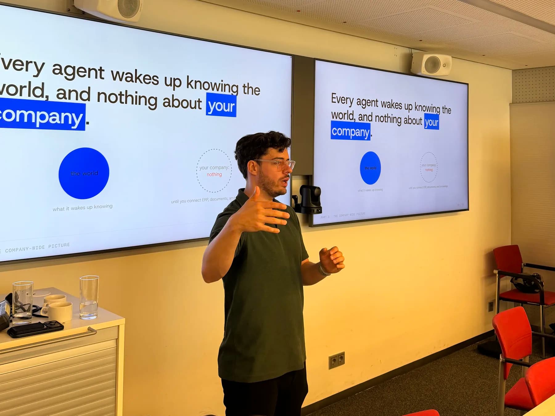 Nik Redl presenting the company-wide picture to executives at the WKO AI workshop in Vienna, two screens behind him reading: every agent wakes up knowing the world, and nothing about your company.